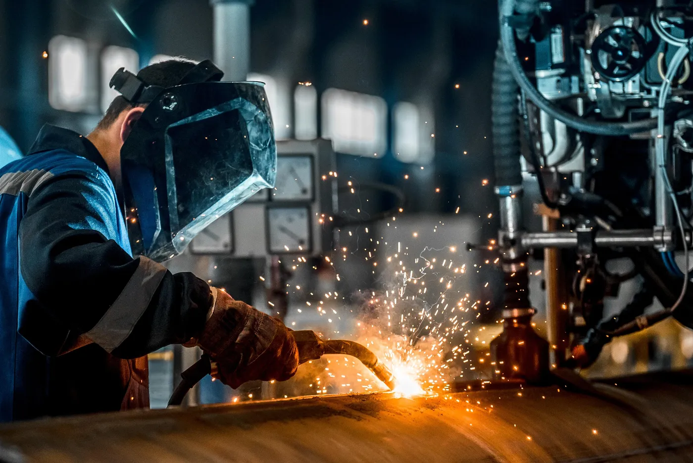 A welder in a protective mask working on a steel pipe, with sparks flying